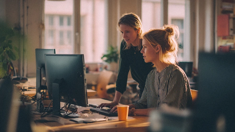 ee-kvinnor-samarbetar Två kvinnor pratar vid en kontorsplats.
